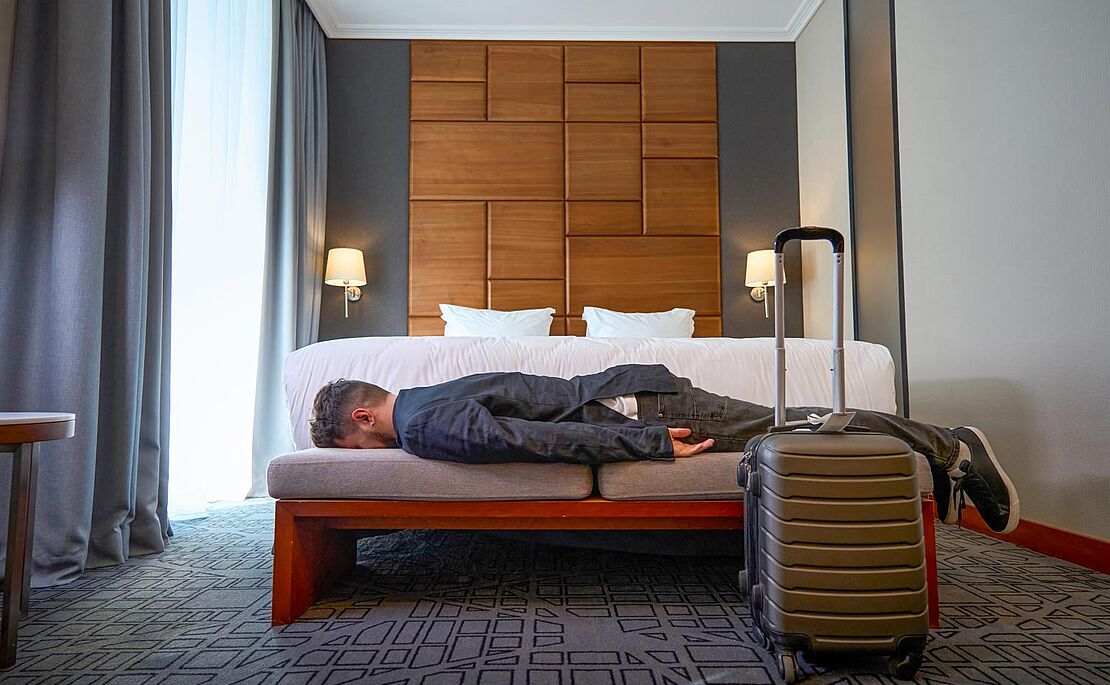Mann liegt erschöpft auf Bett in Hotelzimmer